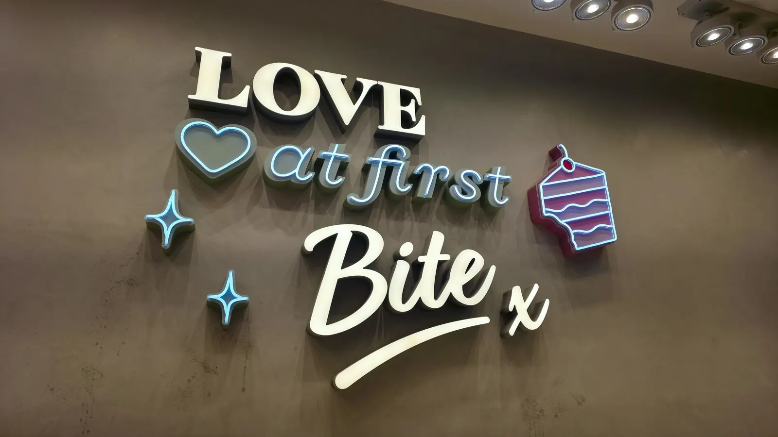 Neon and 3D wall sign reading 'Love at first Bite x' with a heart, sparkles and a cake slice at EL&N London
