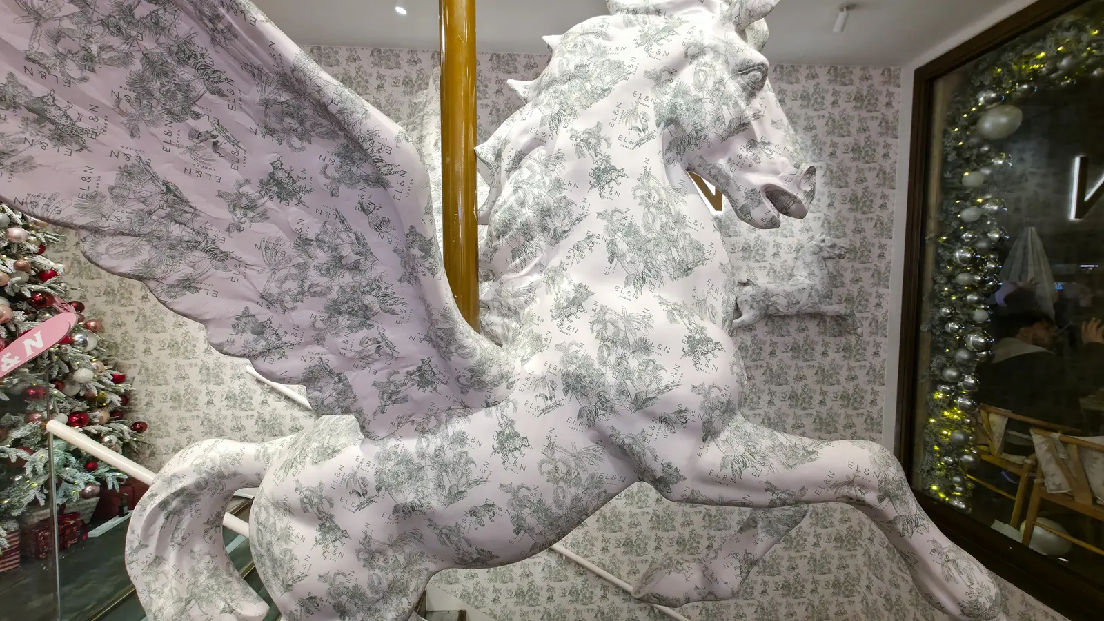 A winged Pegasus statue wrapped in EL&N London's green botanical toile print, beside a decorated Christmas tree