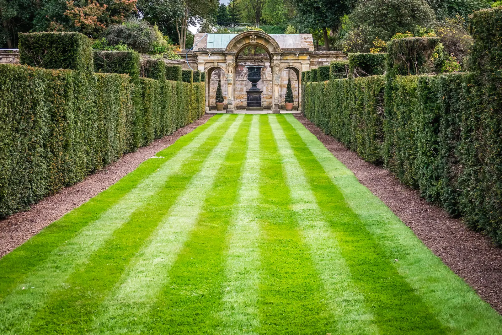 The striped lawn and clipped yew hedges of the Italian Garden at Hever Castle leading to a classical stone loggia and urn