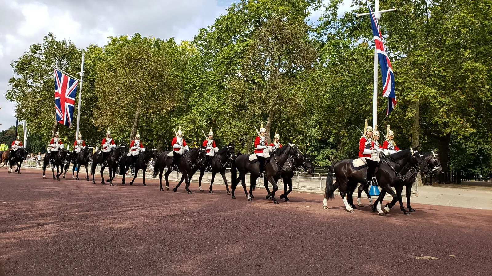Mounted Household Cavalry in red tunics and plumed helmets riding down The Mall past Union flags