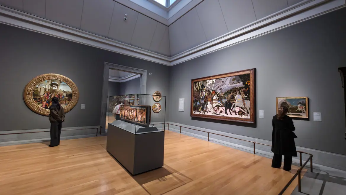 A Sainsbury Wing gallery at the National Gallery, London: Uccello's Battle of San Romano on the wall and Botticelli's gold Adoration tondo, with Pesellino's David panels in a glass case.
