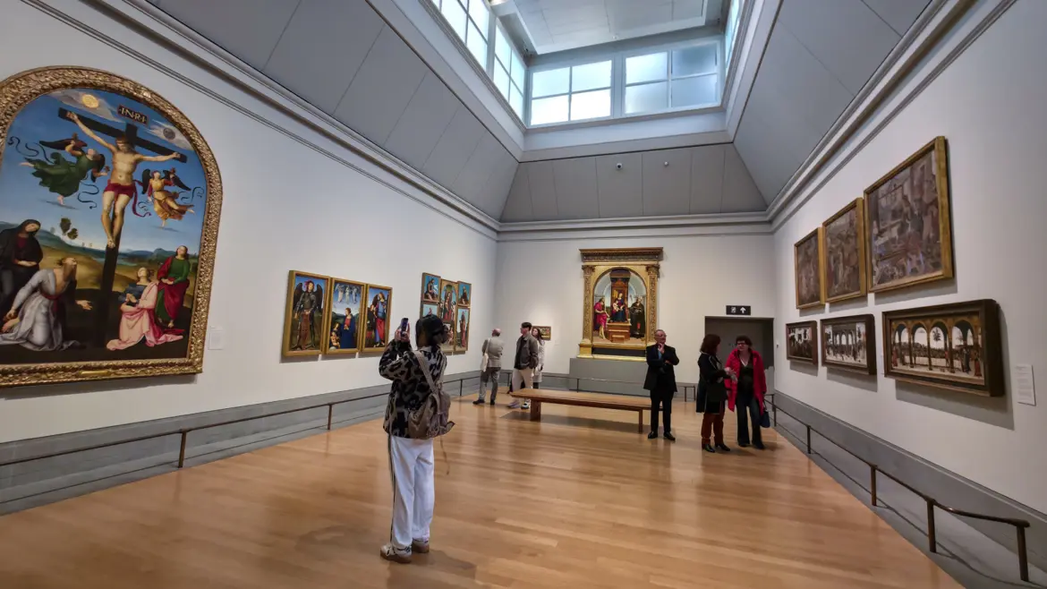 An Umbrian gallery at the National Gallery, London, with Raphael's arched Mond Crucifixion on the left wall and gold-framed altarpieces along the room.