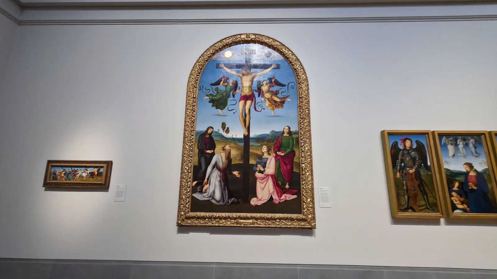 Raphael's Mond Crucifixion at the National Gallery, London, Christ on the cross with two angels and four figures below, in an arched gold frame.