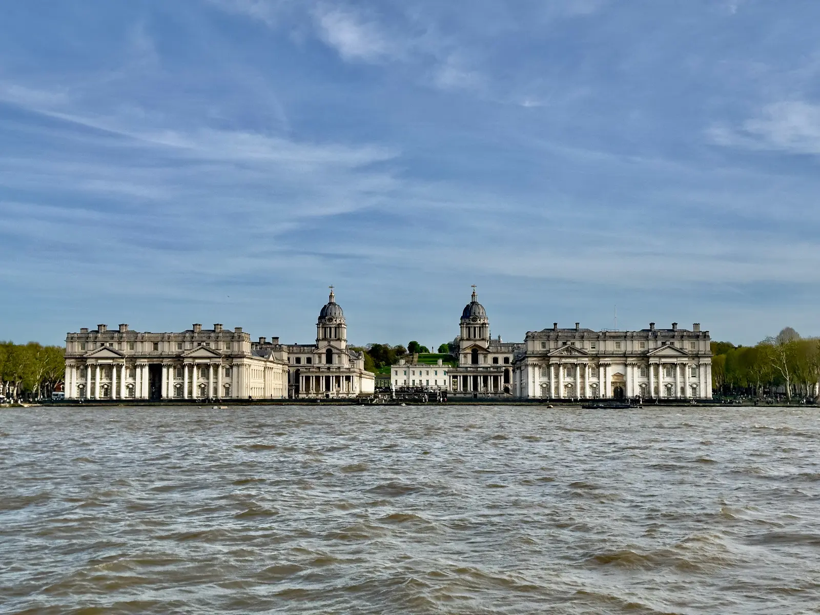The Old Royal Naval College at Greenwich seen across the River Thames, its twin domes flanking the white Queen’s House, with Greenwich Park behind