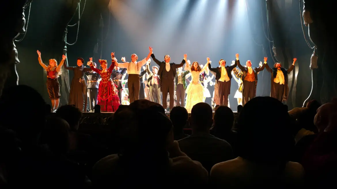 The cast of The Phantom of the Opera taking a curtain call under dramatic lighting, the masked Phantom and Christine at centre stage, His Majesty's Theatre, London