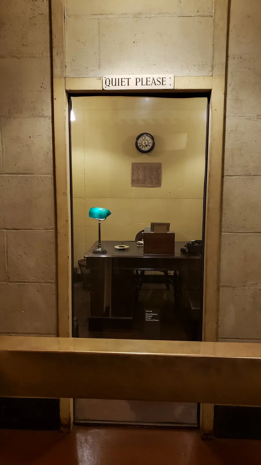 A preserved underground office behind glass at the Churchill War Rooms, London, beneath a "Quiet Please" sign