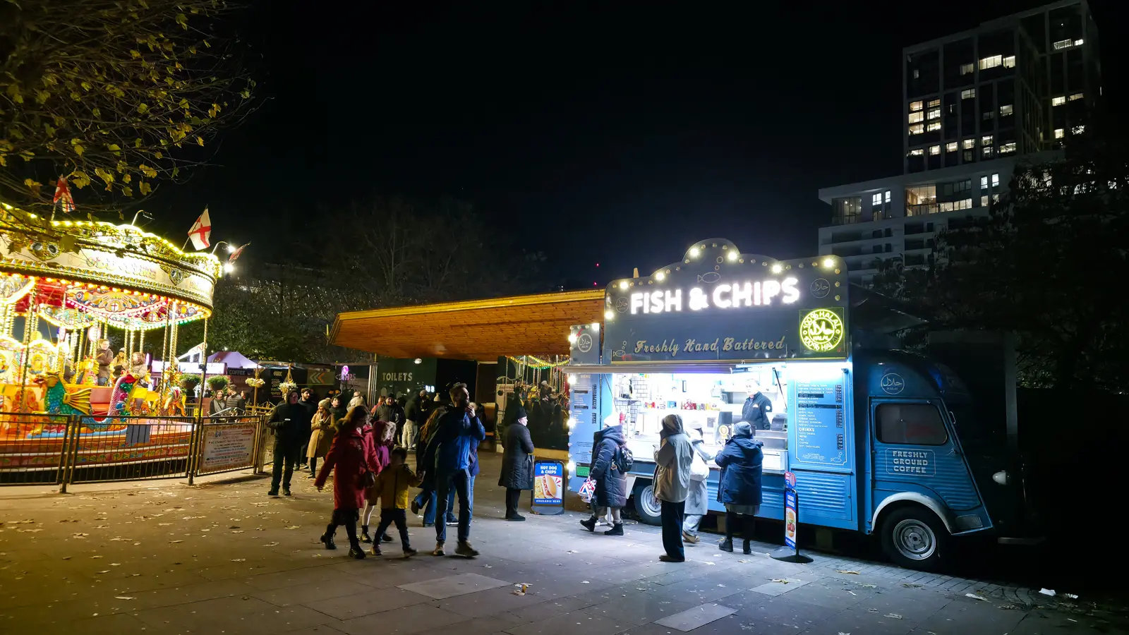 A vintage Citroen H van converted into a brightly lit Fish & Chips stall at night, beside the gold carousel at the Southbank Centre Winter Market, London