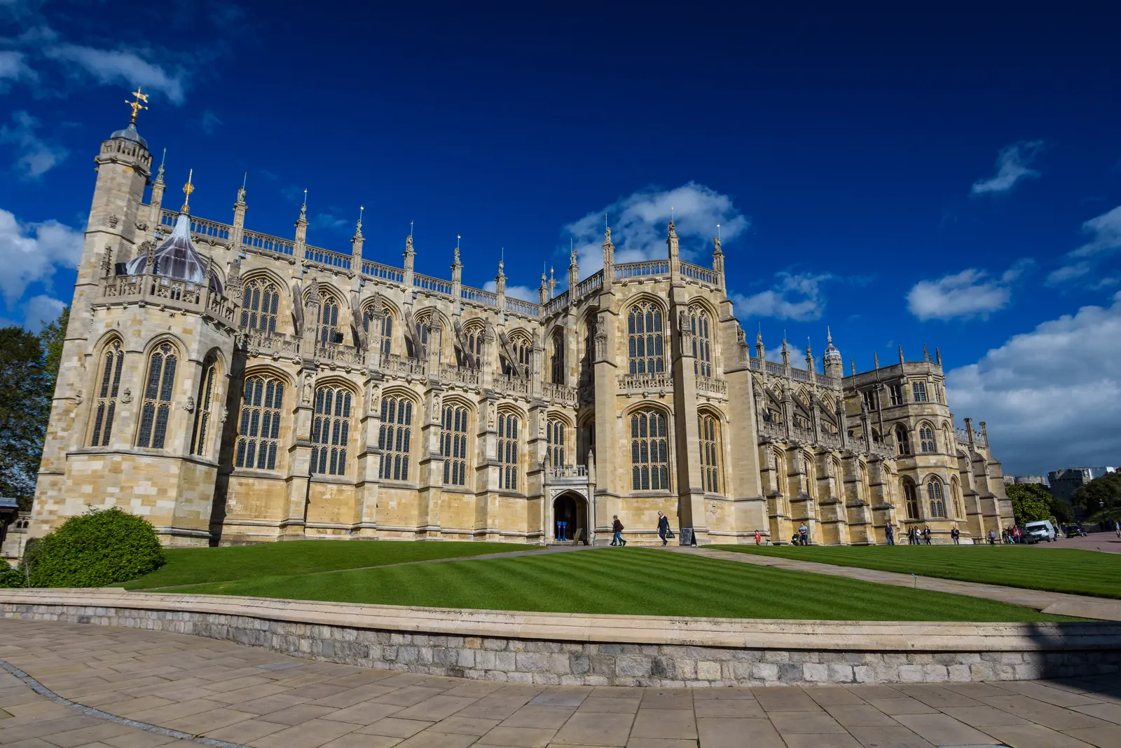 The Gothic exterior of St George’s Chapel at Windsor Castle, its tall traceried windows and pinnacles above a green lawn under a blue sky