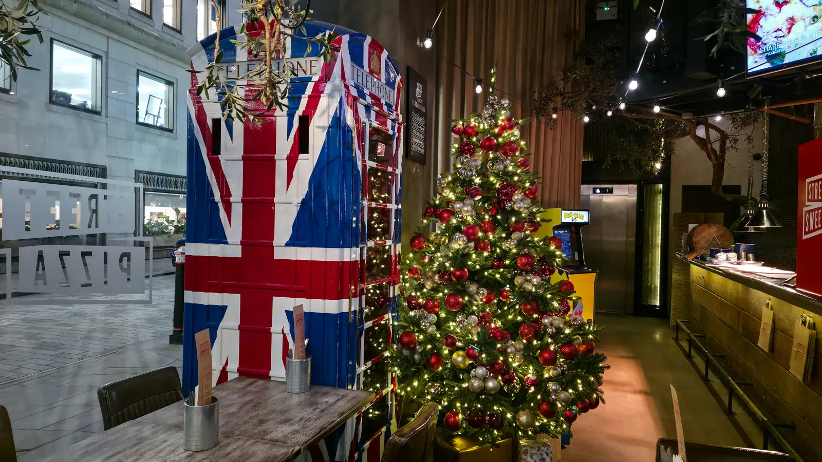 A Union Jack telephone box and a Pac-Man machine beside the Christmas tree at Street Pizza by Gordon Ramsay, London