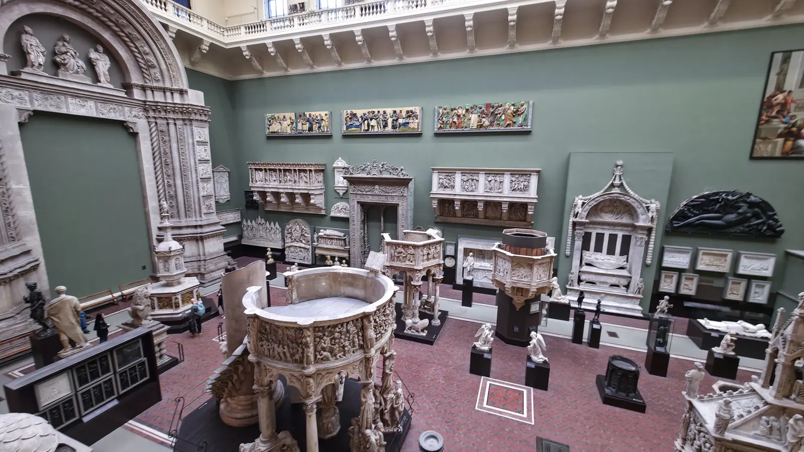 An elevated view over the V&A's Italian Cast Court, with green walls and full-size plaster casts of pulpits, doorways and tomb monuments, London