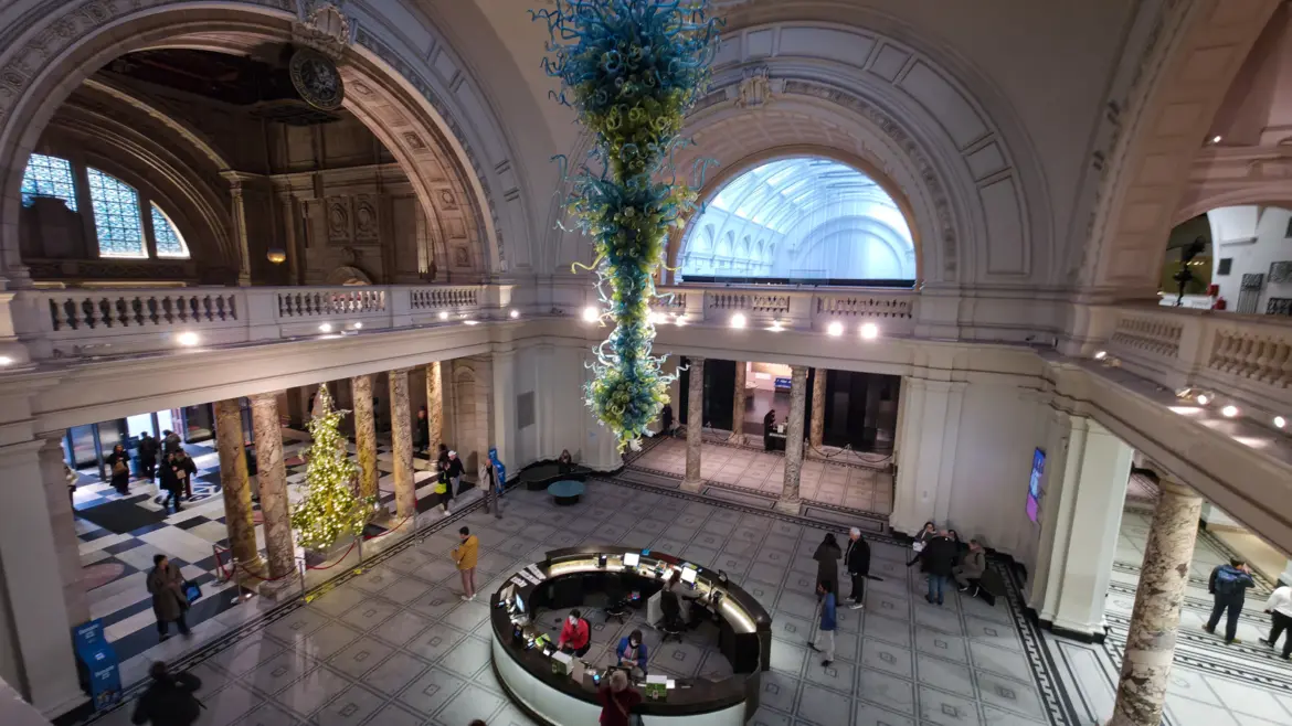The grand entrance rotunda of the V&A with Dale Chihuly's blue and green blown-glass chandelier hanging from the domed ceiling, South Kensington, London