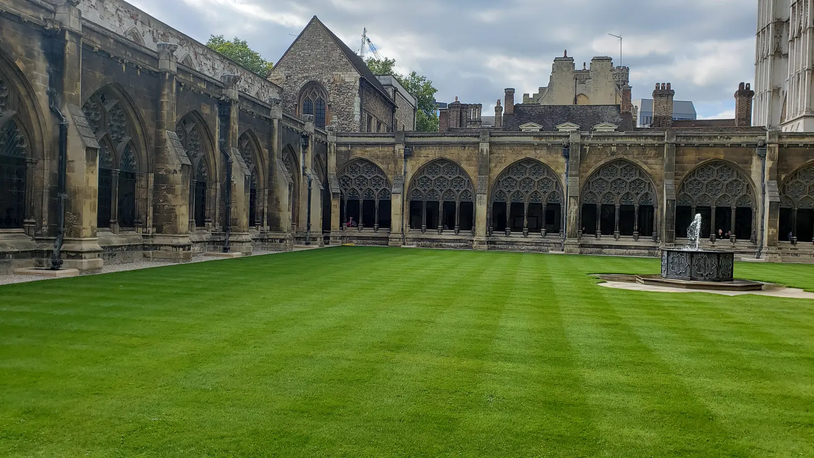 The cloisters of Westminster Abbey, Gothic arcades and tracery around a green garth with a fountain, under a grey sky in London