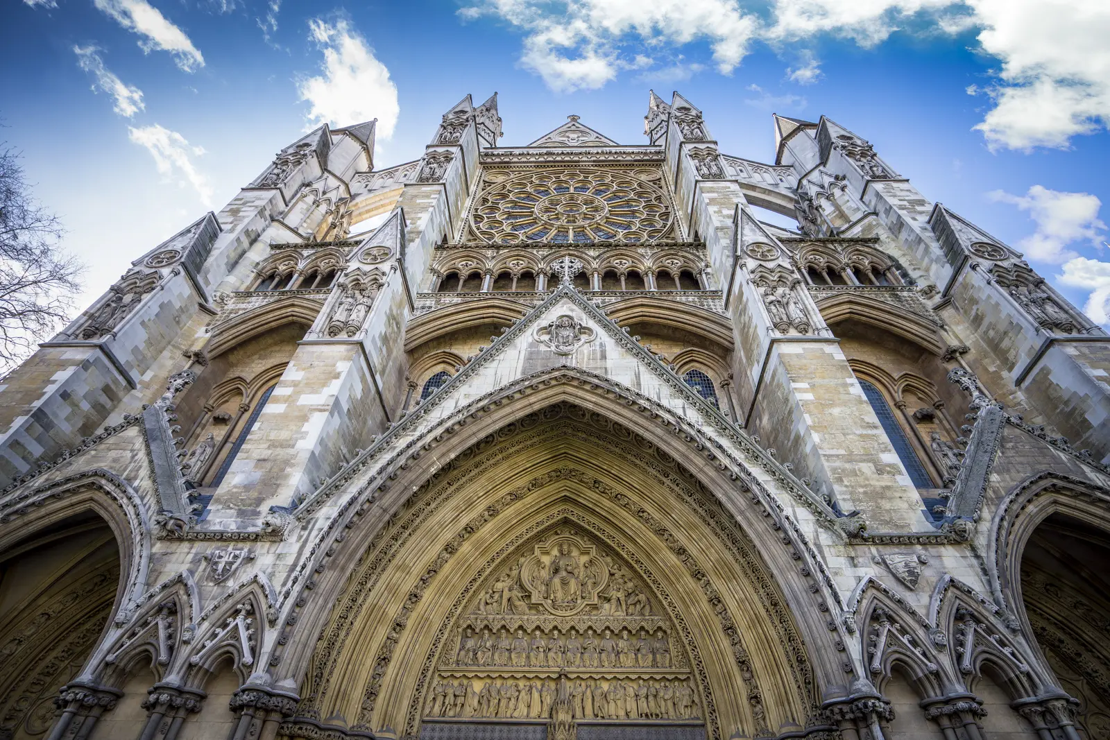 Looking steeply up at the north front of Westminster Abbey, with the rose window and twin turrets against a cloudy blue sky