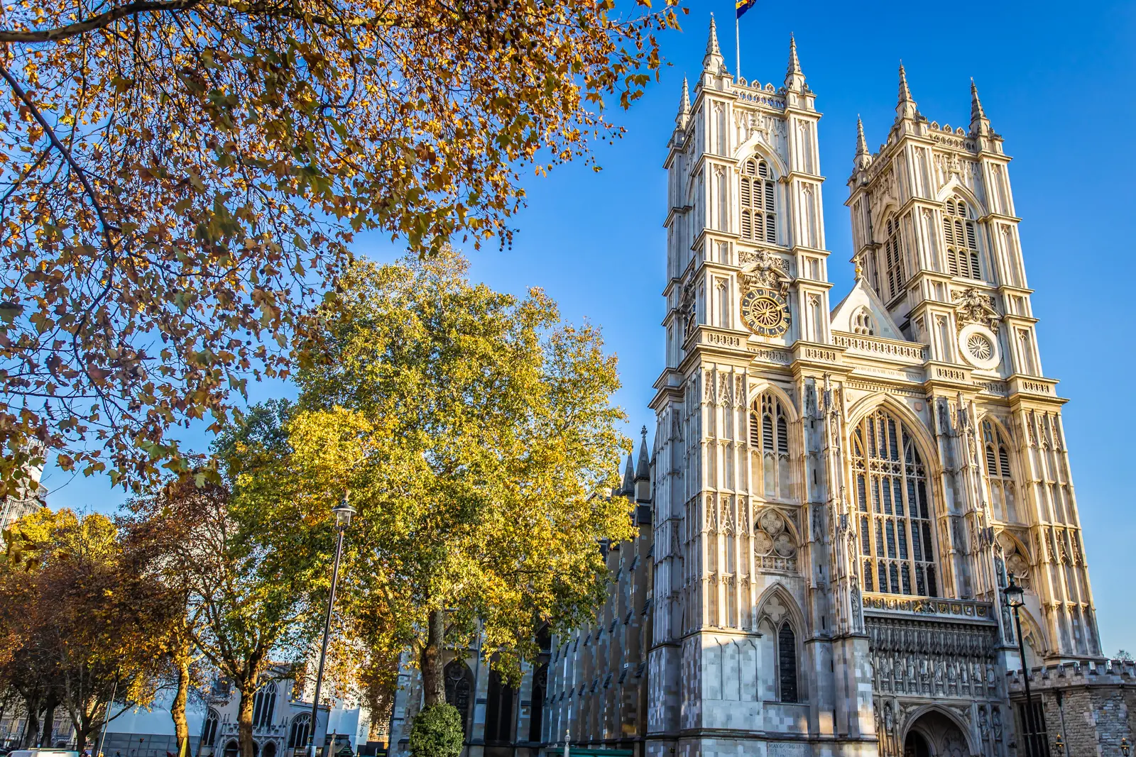 The two pale western towers of Westminster Abbey framed by golden autumn trees against a blue sky