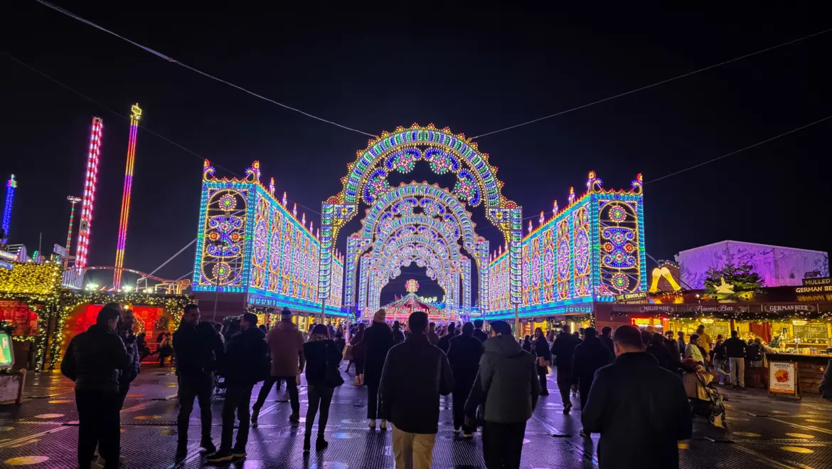 The illuminated entrance arches of Winter Wonderland, Hyde Park, London, glowing over the crowds at night