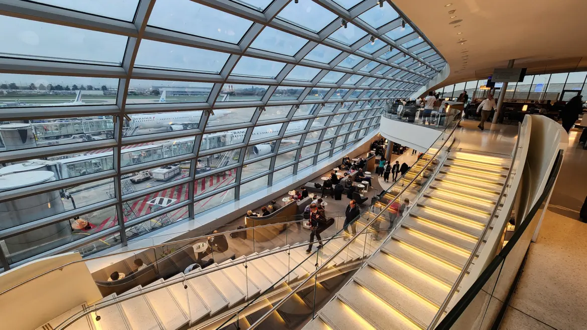 The Air France lounge in Terminal 2F at Paris-Charles de Gaulle, a curved glass wall and staircase above the apron, with Air France and KLM jets outside