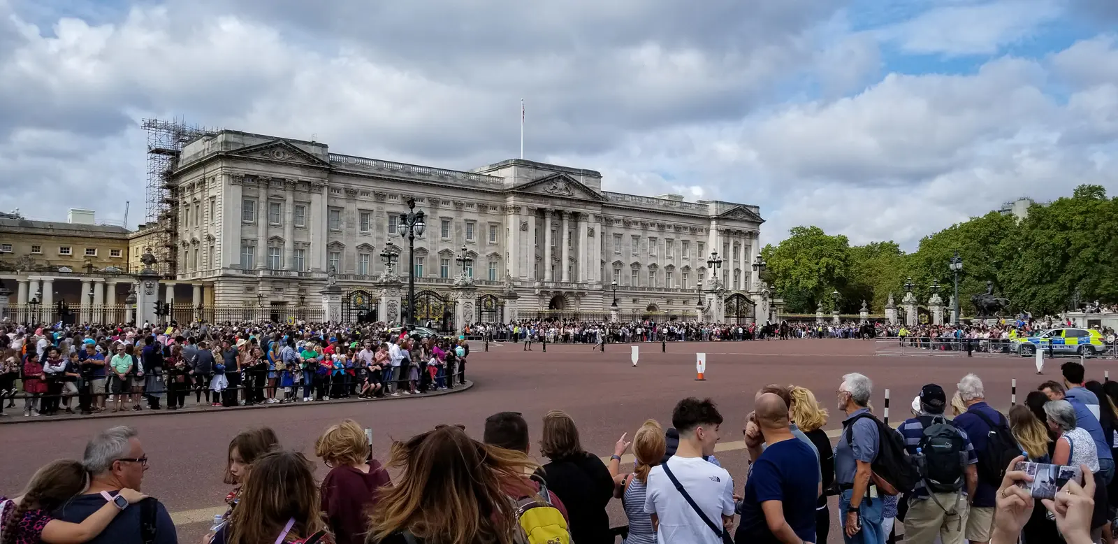 Crowds lining the railings in front of Buckingham Palace in London, waiting for Changing the Guard on a cloudy day