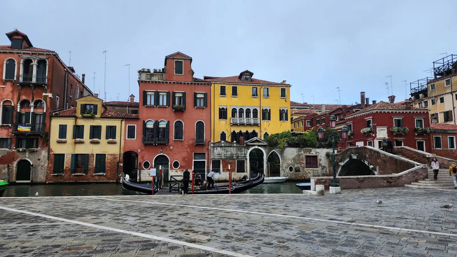 The canal-side edge of Campo Santi Giovanni e Paolo, a gondola at the pier, houses across the water, Venice