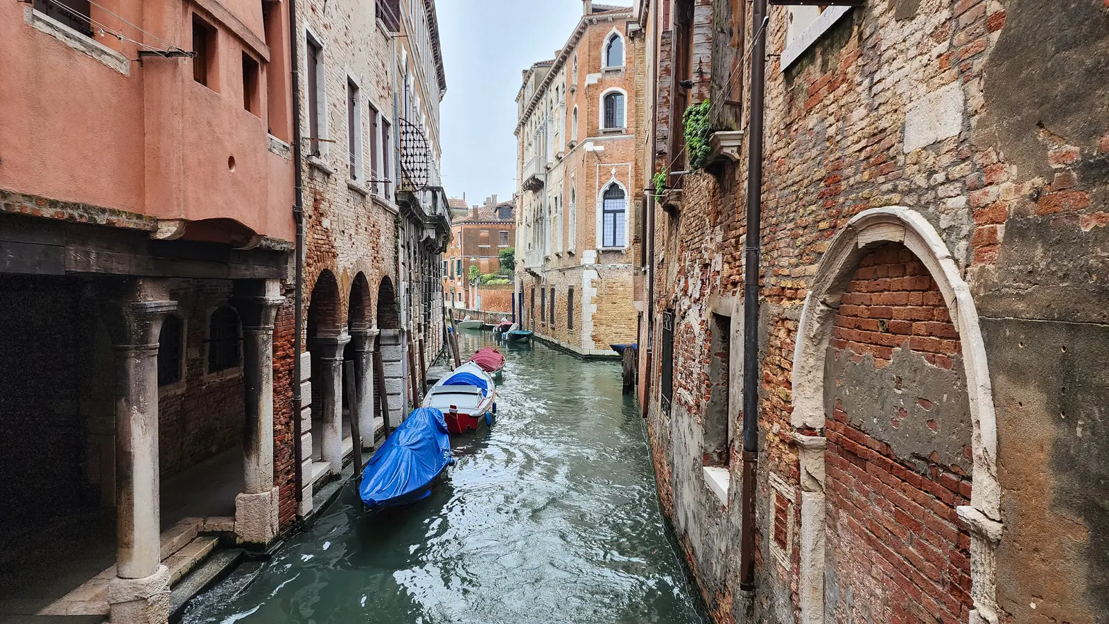 A narrow back canal in Cannaregio with moored boats and worn brick buildings, Venice