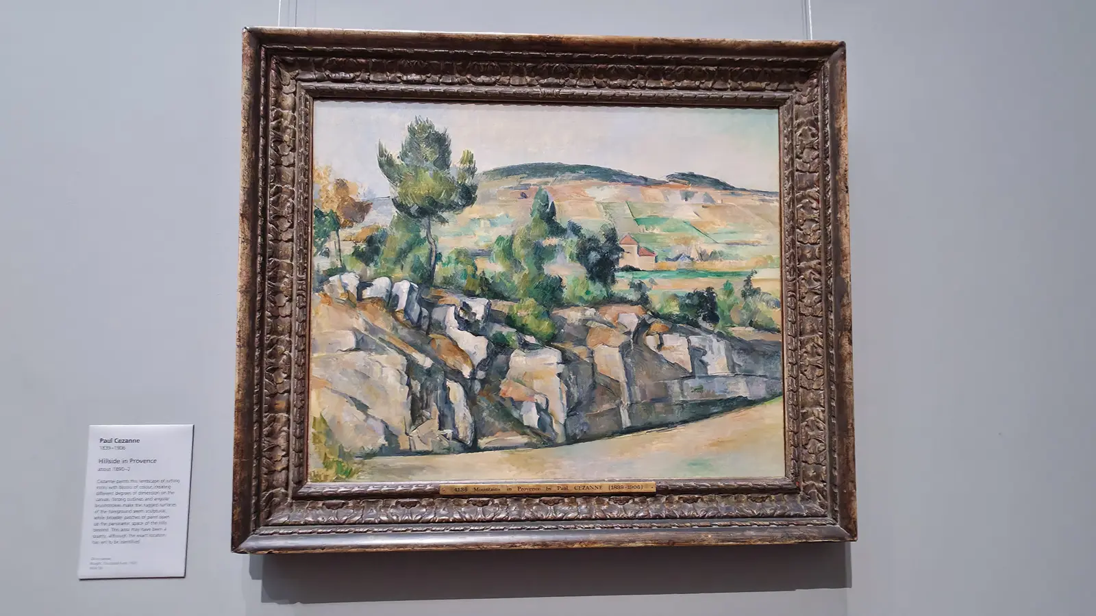 Cézanne's Hillside in Provence, a rocky slope under pines, in an ornate frame at the National Gallery, London