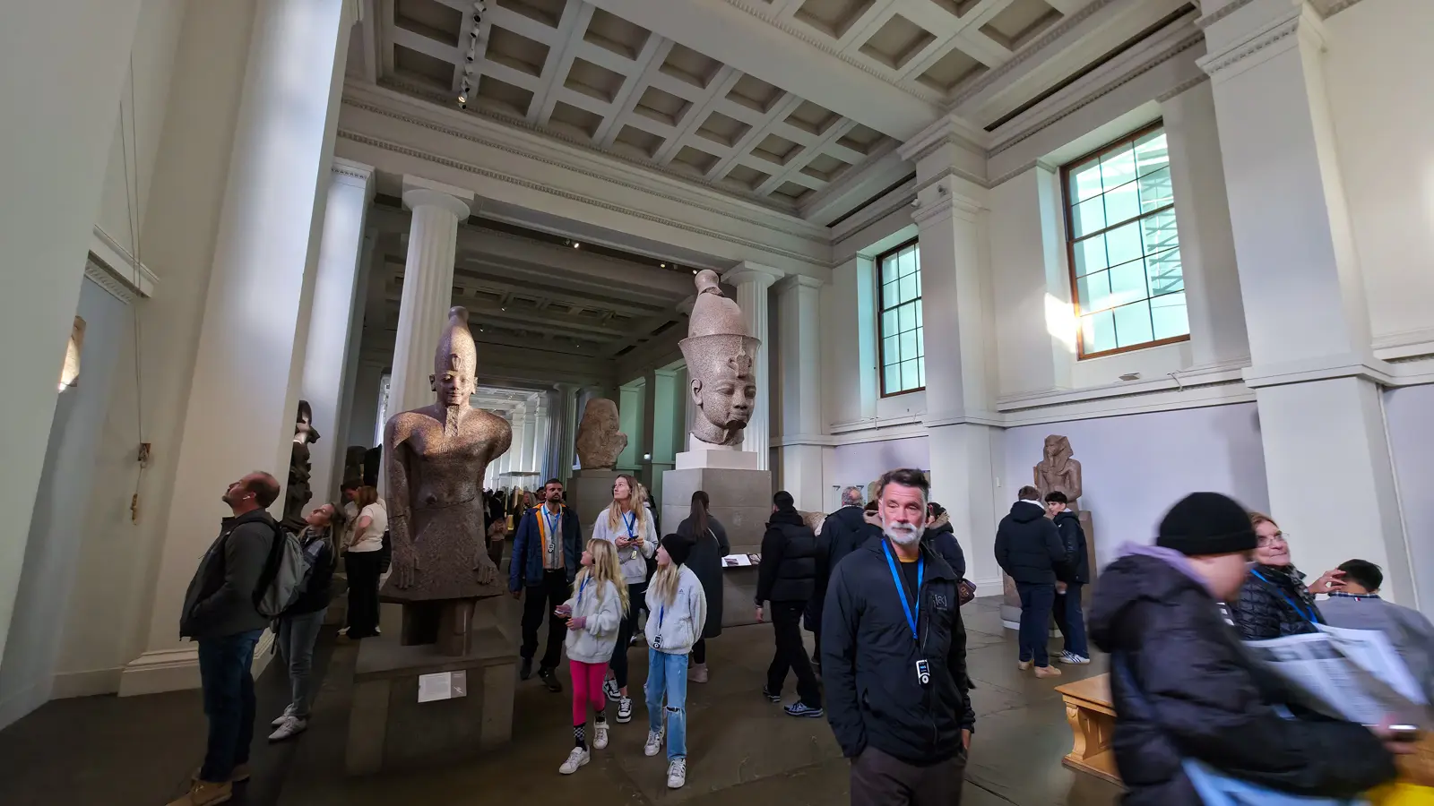 Colossal Egyptian statuary and a pharaoh’s head on plinths in Room 4 of the British Museum, with visitors passing beneath