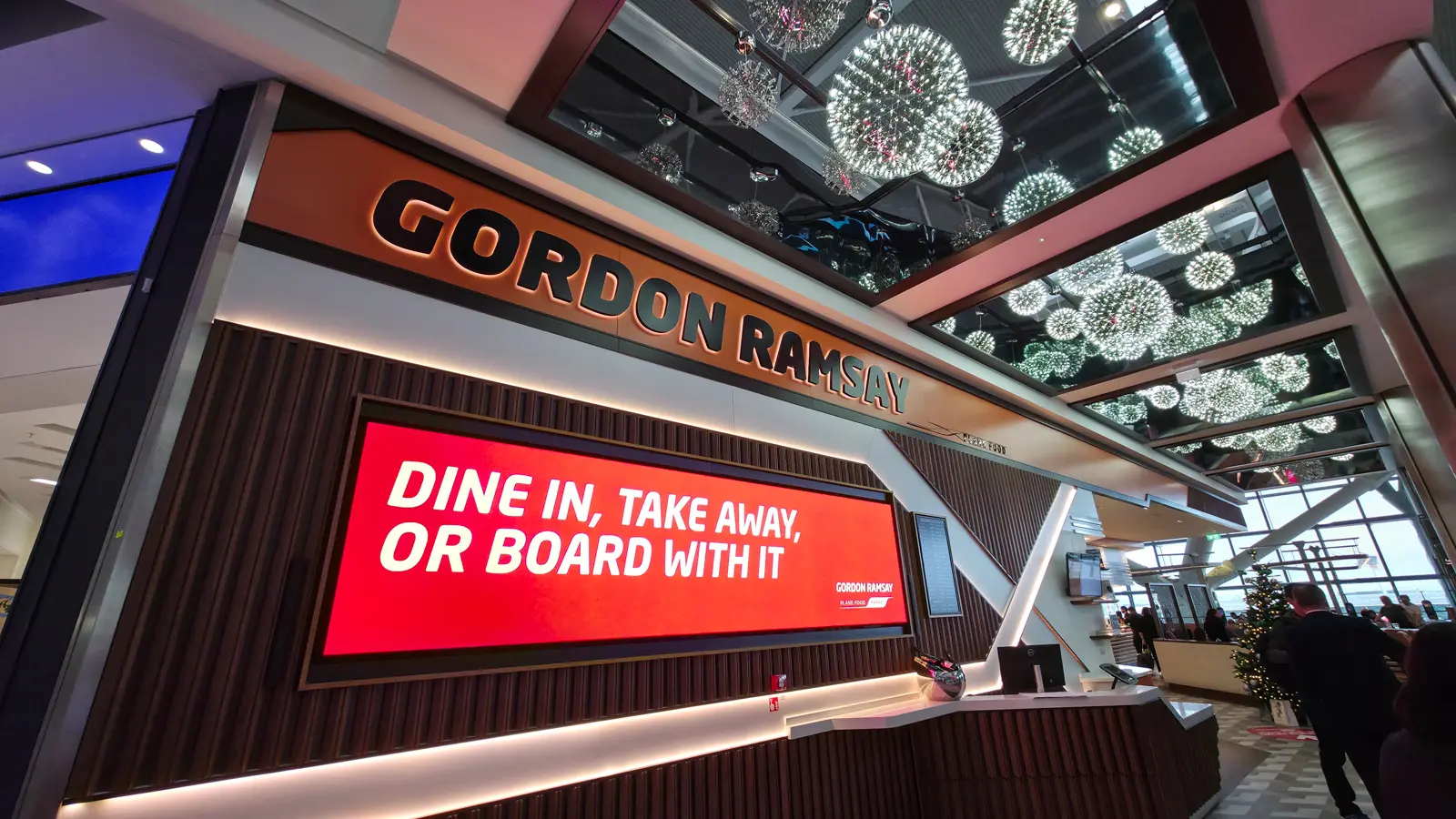 The Gordon Ramsay Plane Food Market sign at Heathrow Terminal 5, reading dine in, take away, or board with it