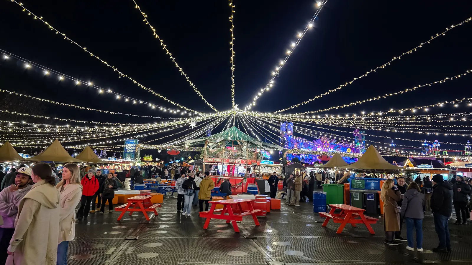 Strings of fairy lights above the stalls and picnic benches at Hyde Park Winter Wonderland in London at night