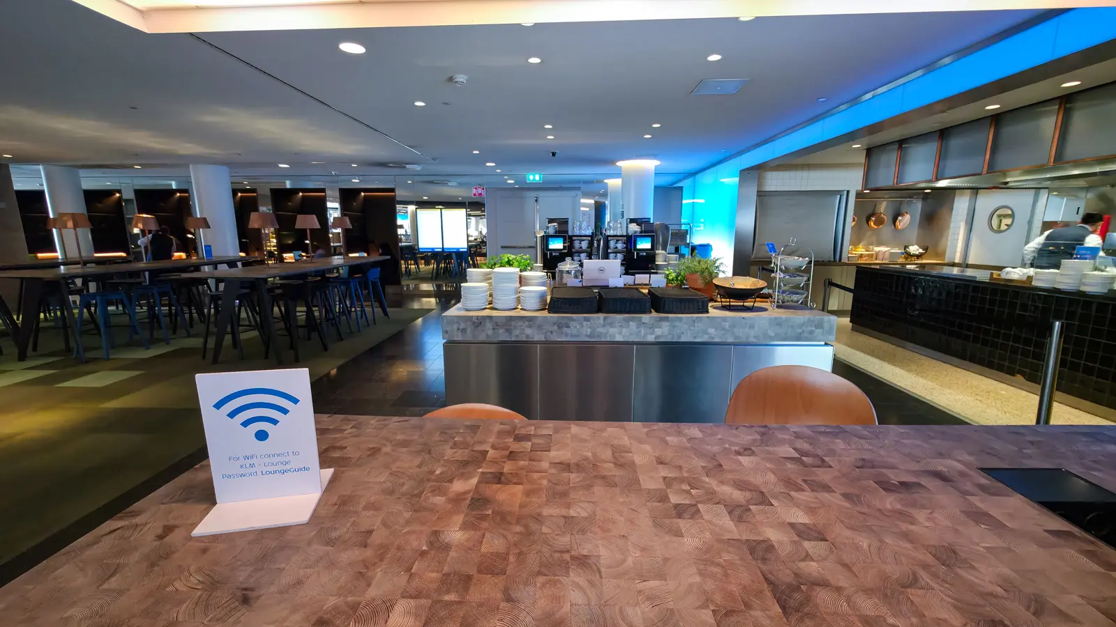 The buffet island and open kitchen in the City area of Crown Lounge 52, with high tables and blue stools alongside, Schiphol