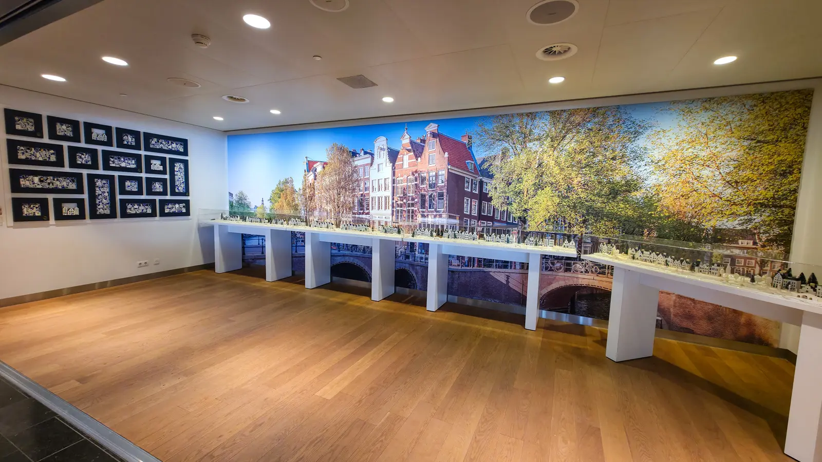 A long display of Delft Blue KLM houses beneath a wall-sized photograph of Amsterdam canal houses, Crown Lounge 52, Schiphol