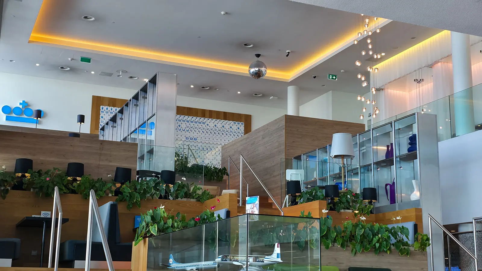 The wooden Dutch Mountain staircase inside Crown Lounge 52, with display cabinets, planting and a mirror ball overhead, Schiphol