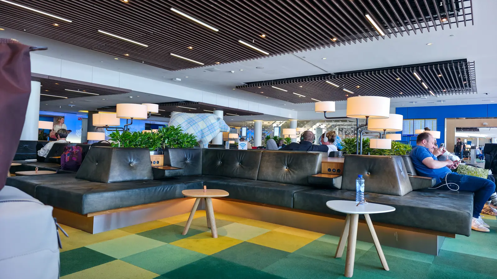 Leather benches and green chequered carpet in the Polder area of Crown Lounge 52, with a fabric sheep standing among the seating, Schiphol
