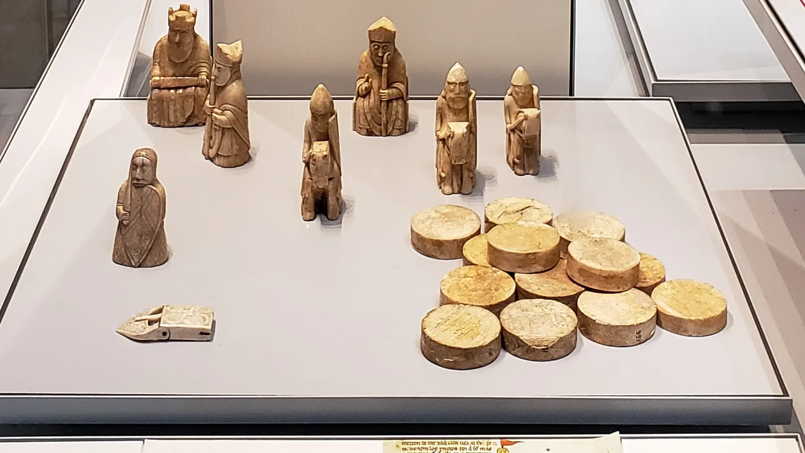 Lewis Chessmen panel with loose kings, bishops and warders, round gaming counters and the ivory belt buckle, British Museum