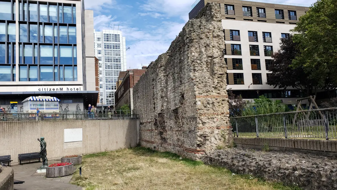 A tall section of Roman and medieval London Wall at Tower Hill, with a bronze statue of Trajan and modern buildings behind