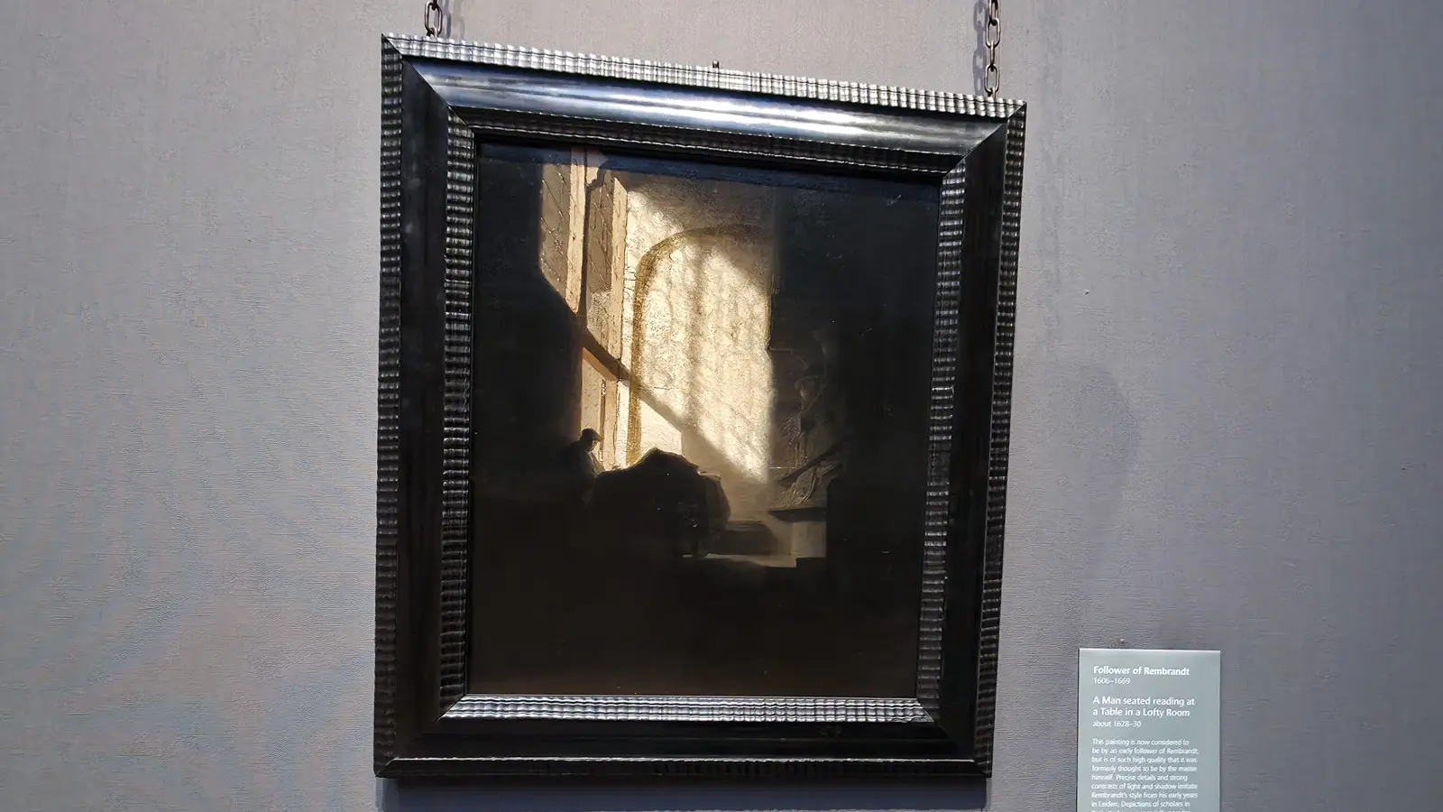 A Man seated reading at a Table in a Lofty Room, by a follower of Rembrandt, a scholar in a sunlit library, National Gallery, London.