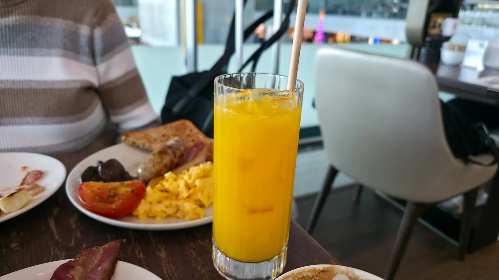 A tall glass of fresh orange juice beside a cooked breakfast at Gordon Ramsay Plane Food Market, Heathrow Terminal 5