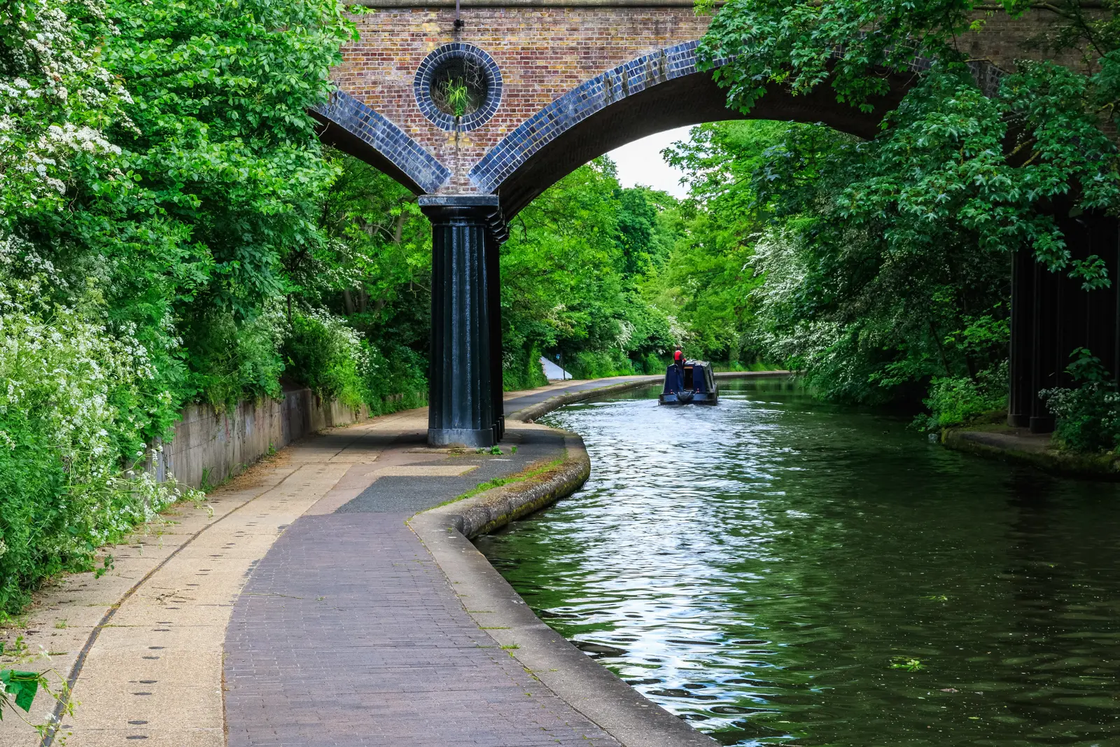 A narrowboat passing under a brick bridge on Regent's Canal, beside the towpath near Regent's Park