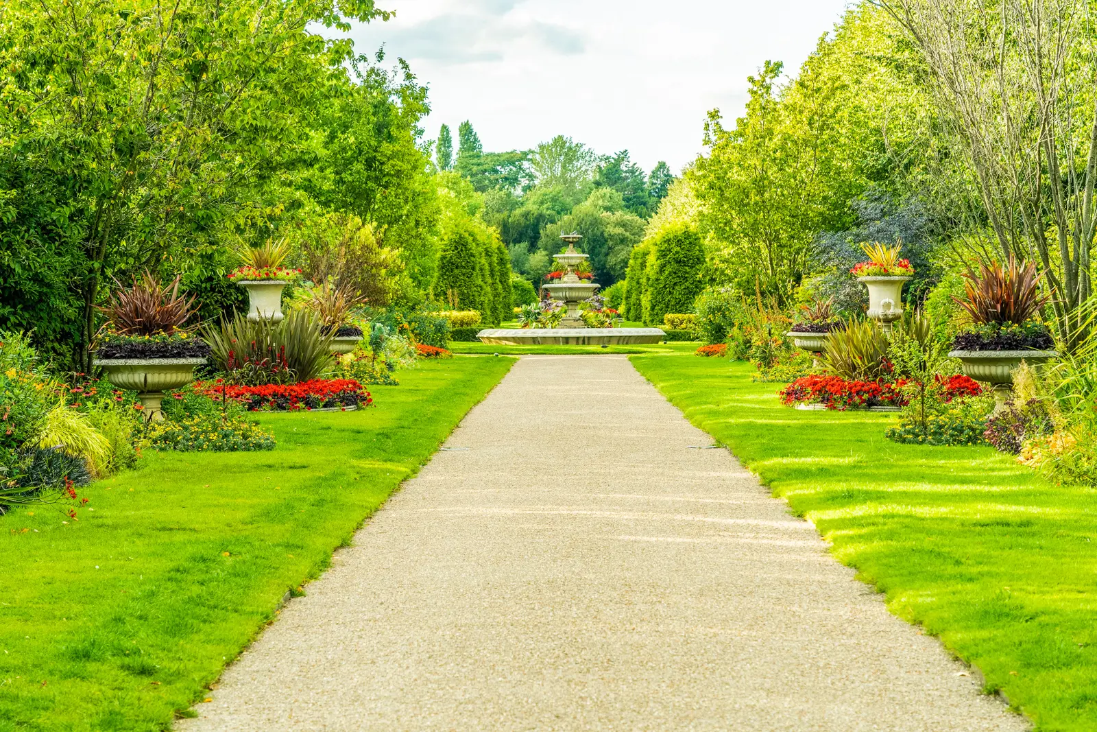 A gravel path in the Avenue Gardens leads to a tiered fountain, framed by urns and red summer bedding
