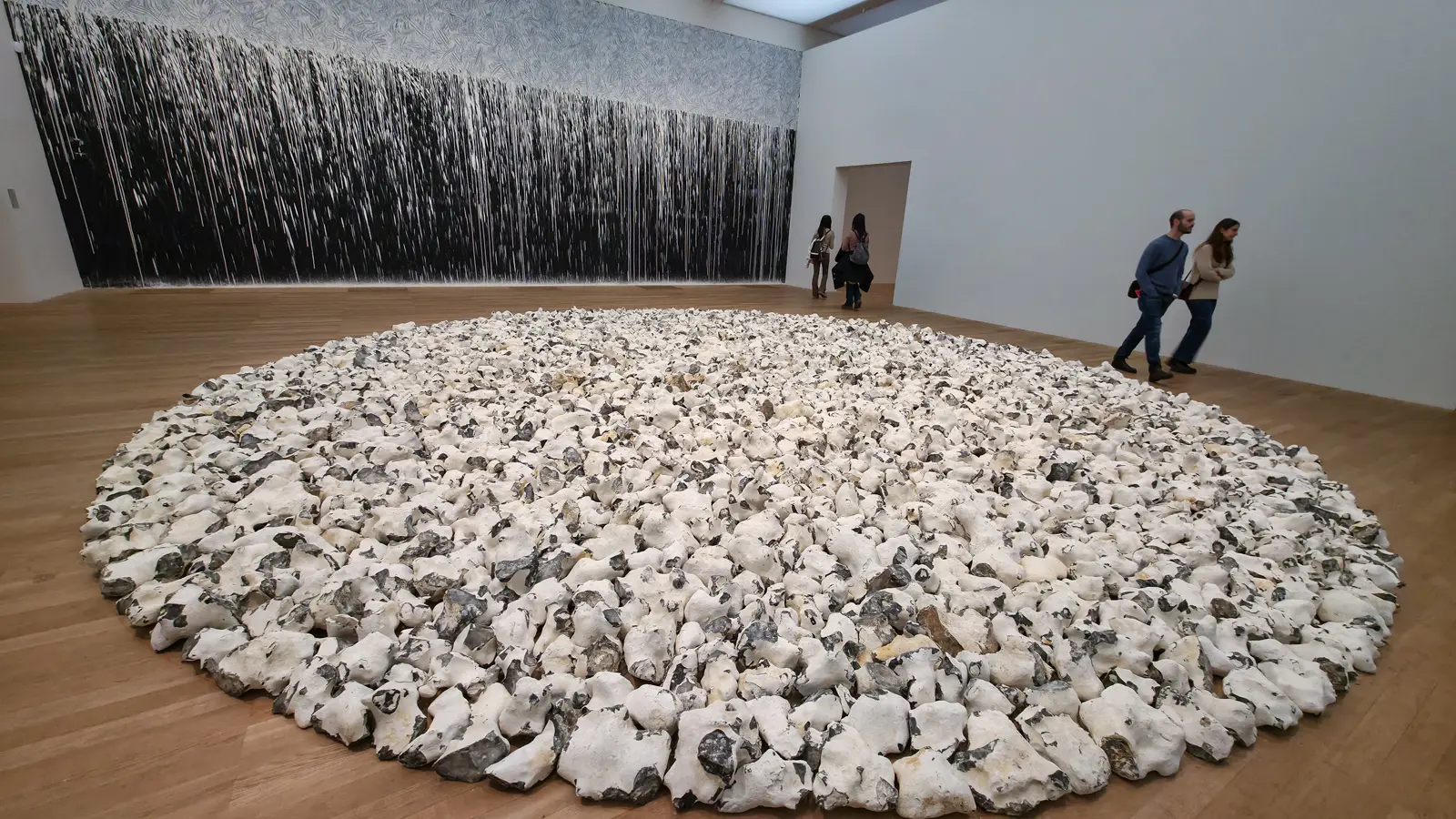 A circle of white stones on the gallery floor at Tate Modern with a dark poured wall work behind, from ARTIST ROOMS: Richard Long