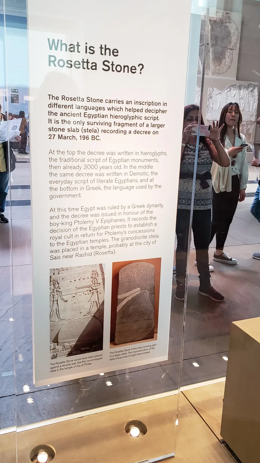 The British Museum’s interpretation panel beside the Rosetta Stone, reflecting visitors photographing through the glass