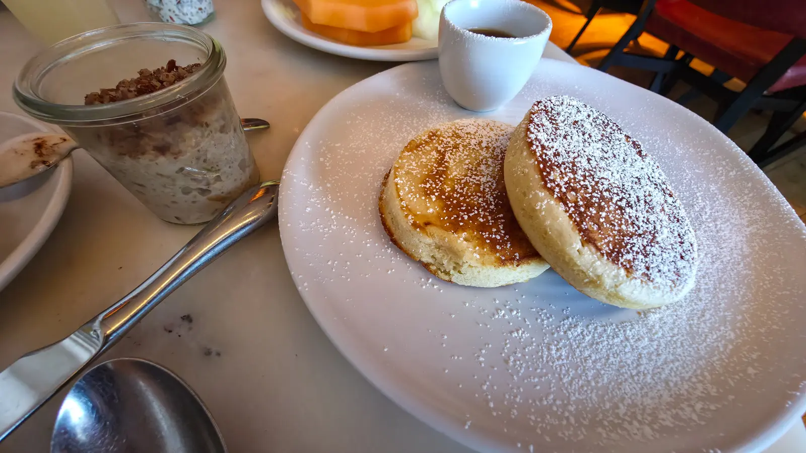 Buttermilk pancakes dusted with icing sugar at Sea Containers Restaurant, with a jar of bircher-style muesli and melon, South Bank London