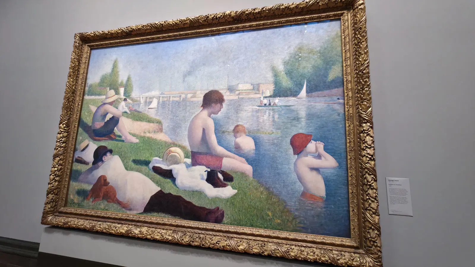 Seurat's Bathers at Asnières, men and boys on a riverbank in the sun, seen close in its gold frame