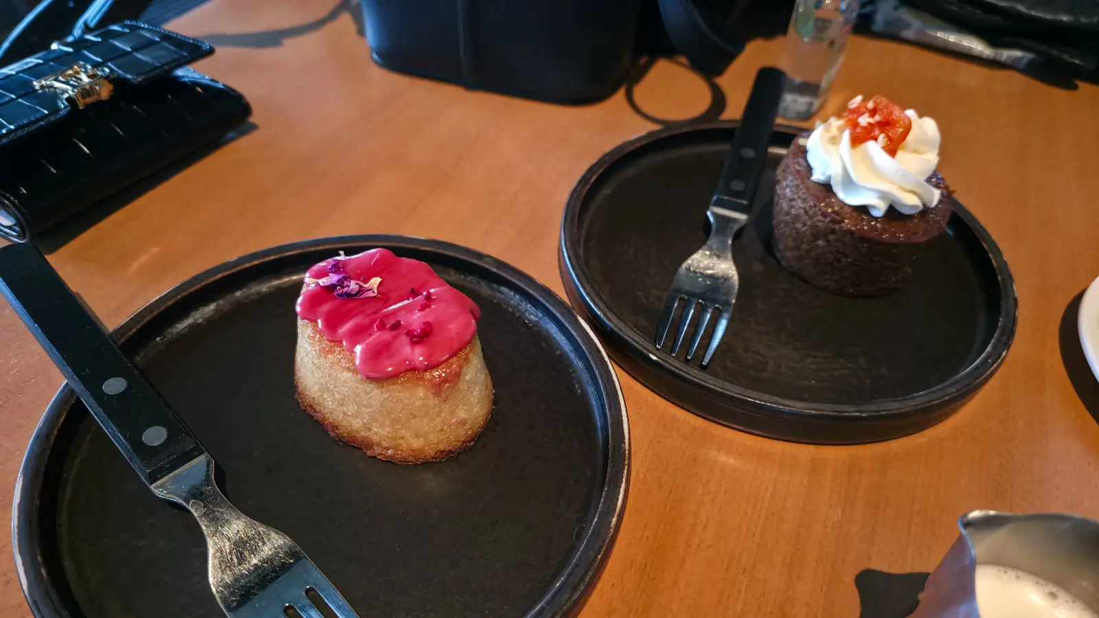 Two desserts on dark plates at the Level 10 café at Tate Modern, one topped with pink icing and petals, the other with cream