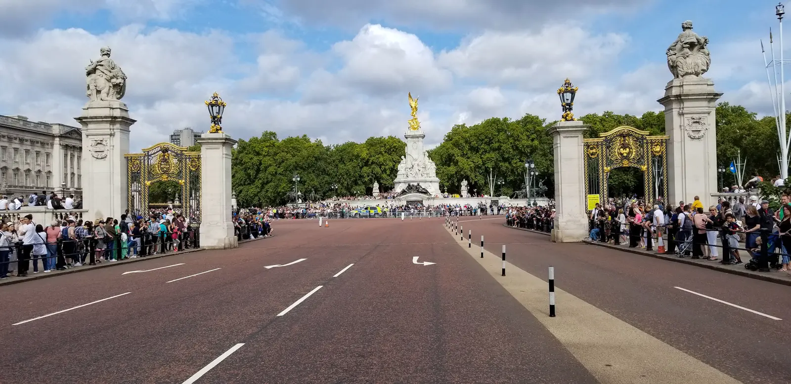 The Australia Gate pier and the white marble Victoria Memorial seen from the Mall, with crowds gathered behind barriers, London.