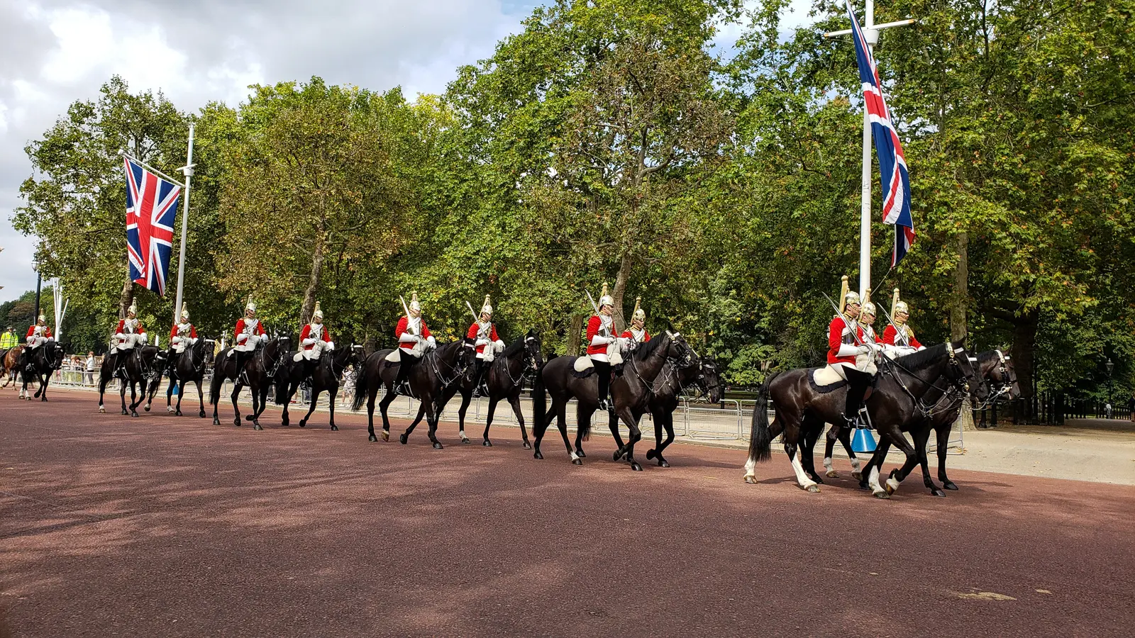Household Cavalry troopers in scarlet tunics and plumed helmets riding in column down the Mall past Union flags, London.