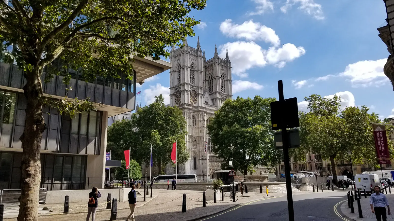 The twin west towers of Westminster Abbey in London, seen from street level with trees and flags in the foreground