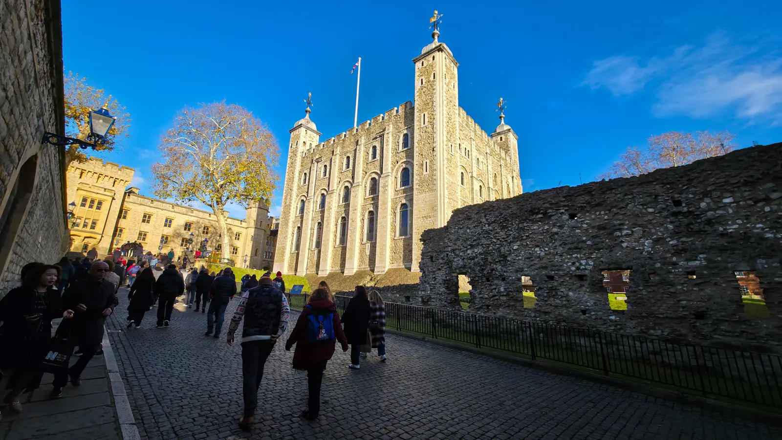 The White Tower at the Tower of London in winter sunshine, with visitors walking the cobbled path beside the inner wall