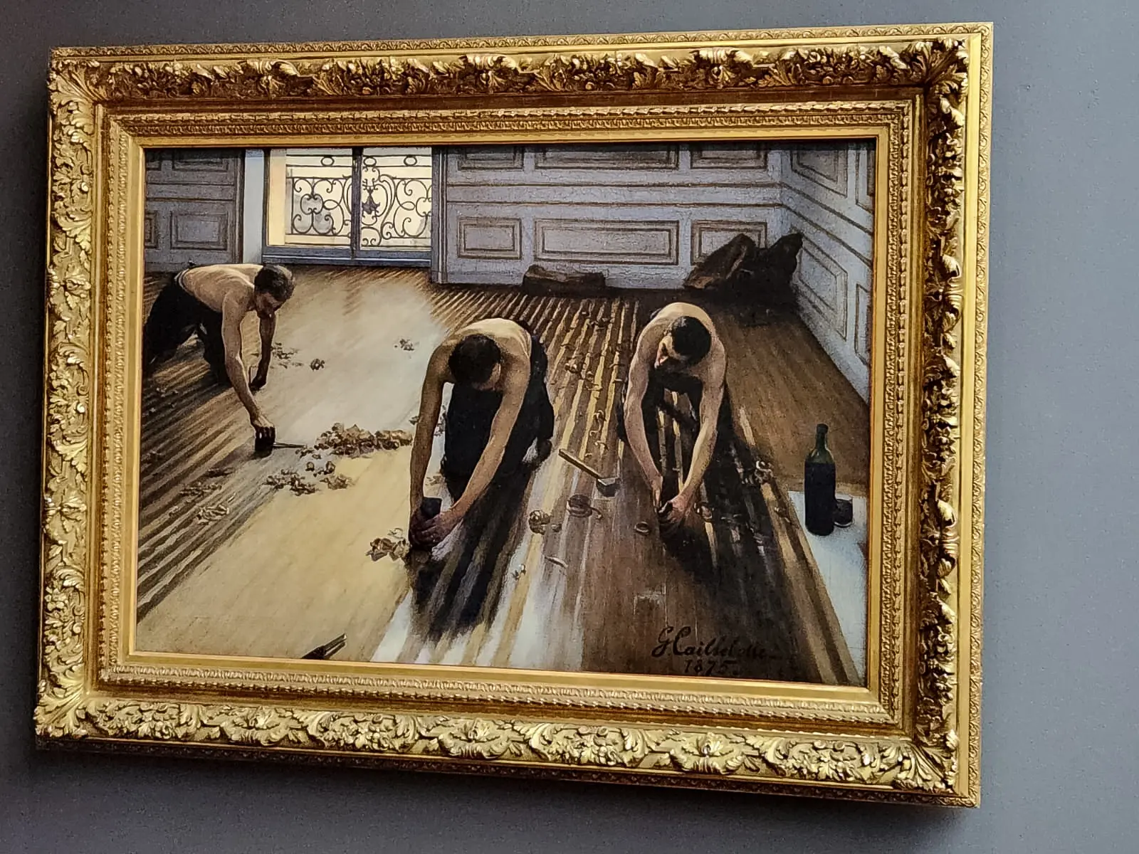 Caillebotte’s The Floor Scrapers at the Musée d’Orsay, three bare-backed men planing floorboards in an empty panelled room