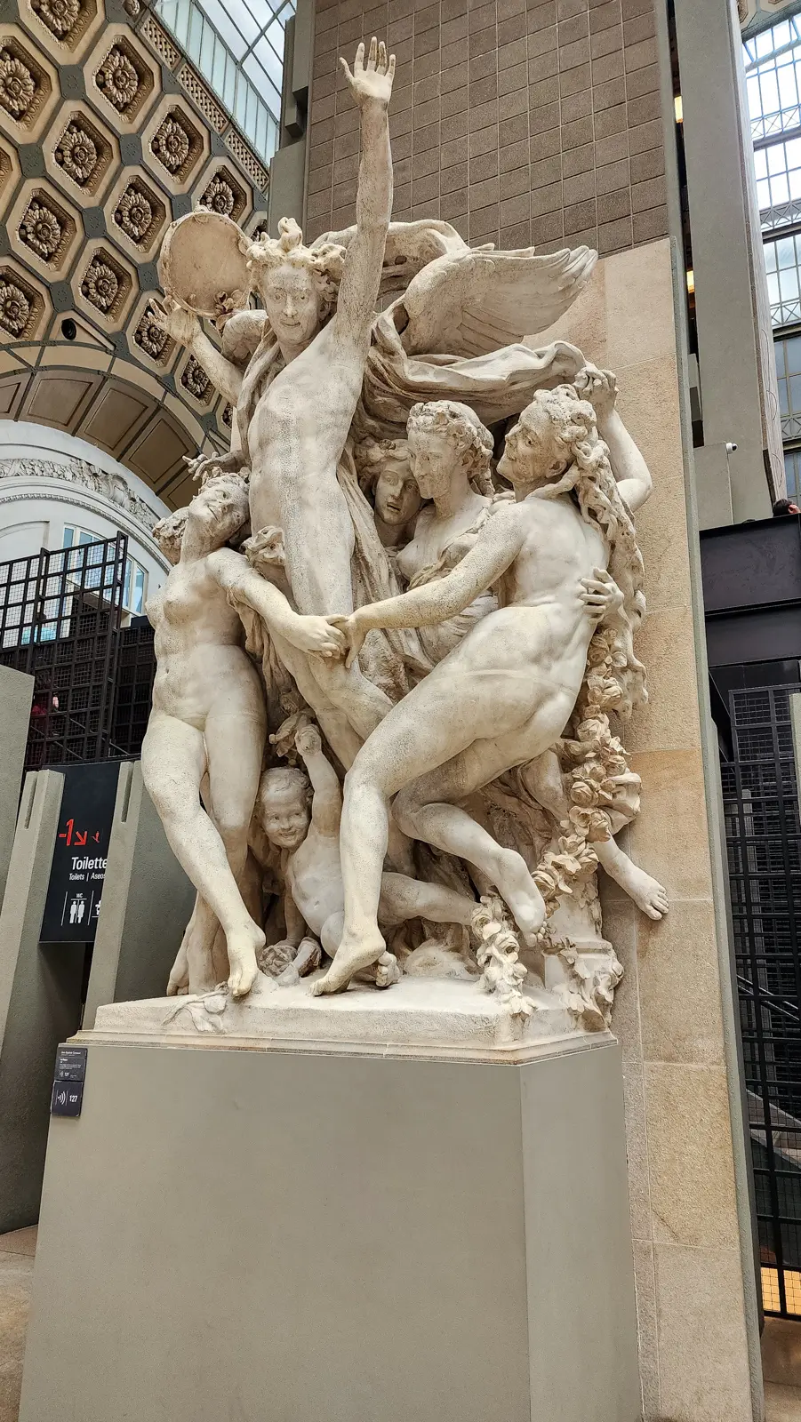 Carpeaux’s La Danse at the Musée d’Orsay, a group of laughing stone figures circling a central raised arm, set against a brick pier
