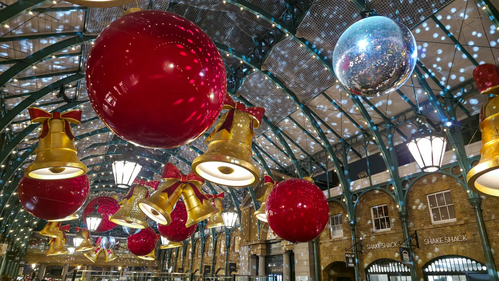The covered market at Covent Garden dressed for Christmas, with giant red baubles, gold bells and a mirror ball under the glass roof