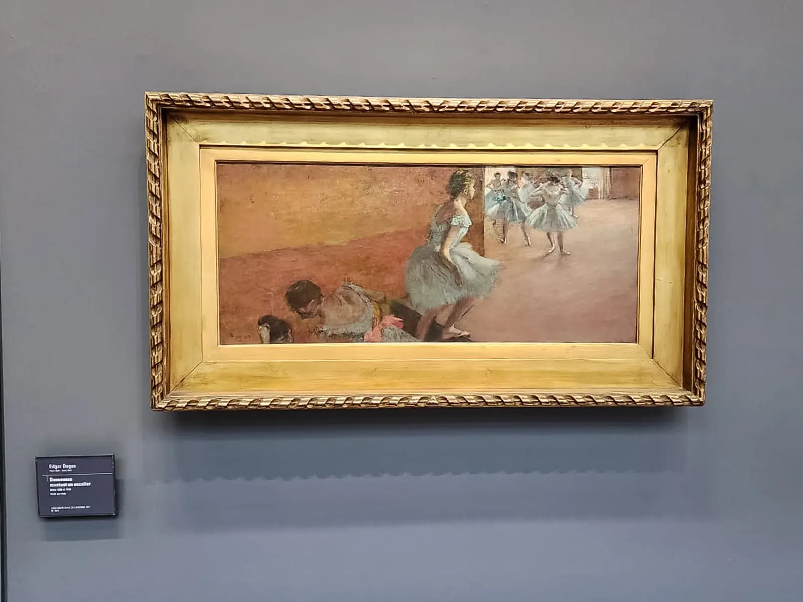 Degas’s Dancers Climbing a Staircase at the Musée d’Orsay, a wide horizontal canvas in a pale gilt frame on a grey wall